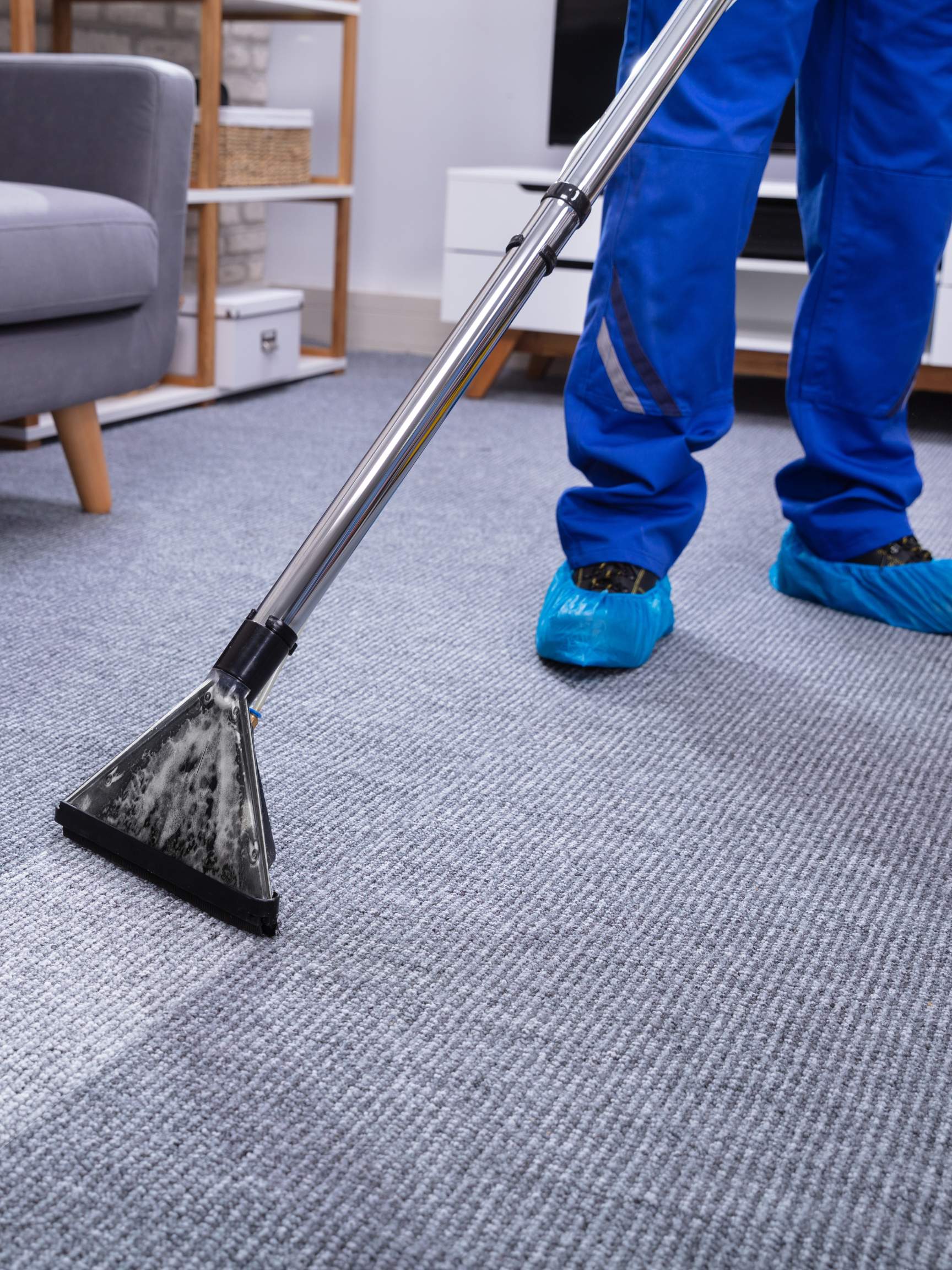 a person using an electronic cleaning machine to clean a light grey carpet. the person is wearing protective waterproof blue footies and clotihing