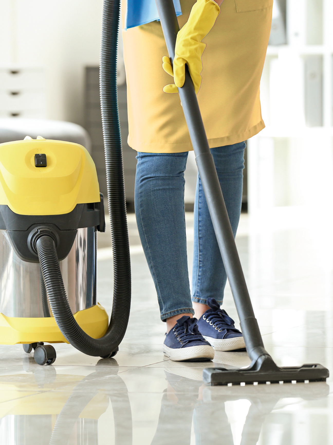 a woman wearing a yellow apron using an electronic mopping machine in the process of mopping a white floor
